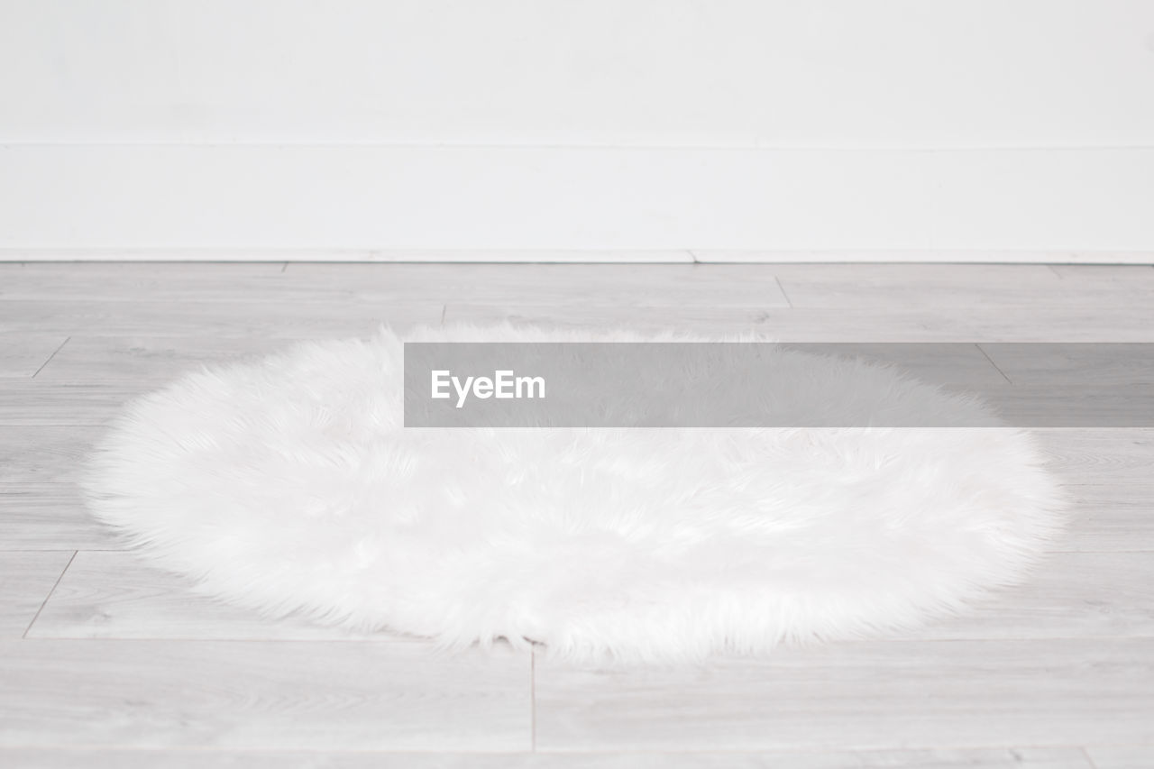 White round fluffy rug carpet lying on floor by white wall at home. background mockup for design