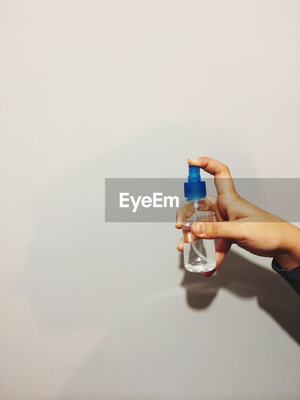 Close-up of hand holding spray bottle against wall