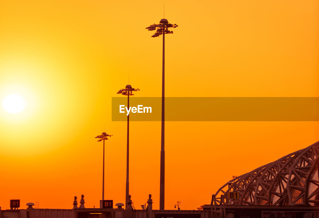 Tall electric pylon in the airport at sunset with an orange sky. spotlights pole at the airfield. 