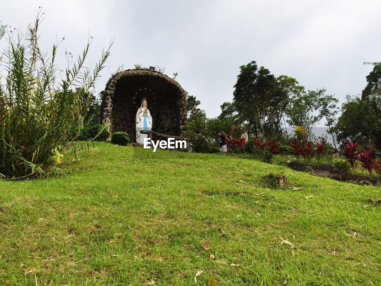 Low angle view of virgin mary on grassy hill against sky