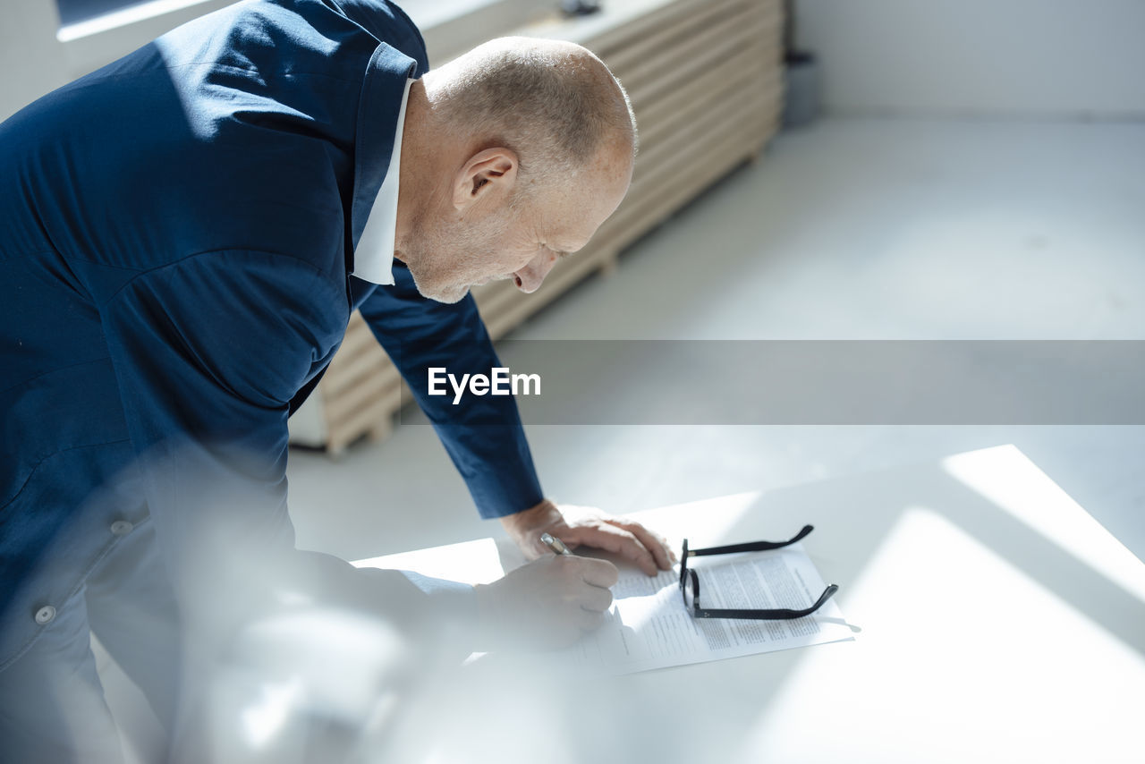 Senior businessman writing on document at desk