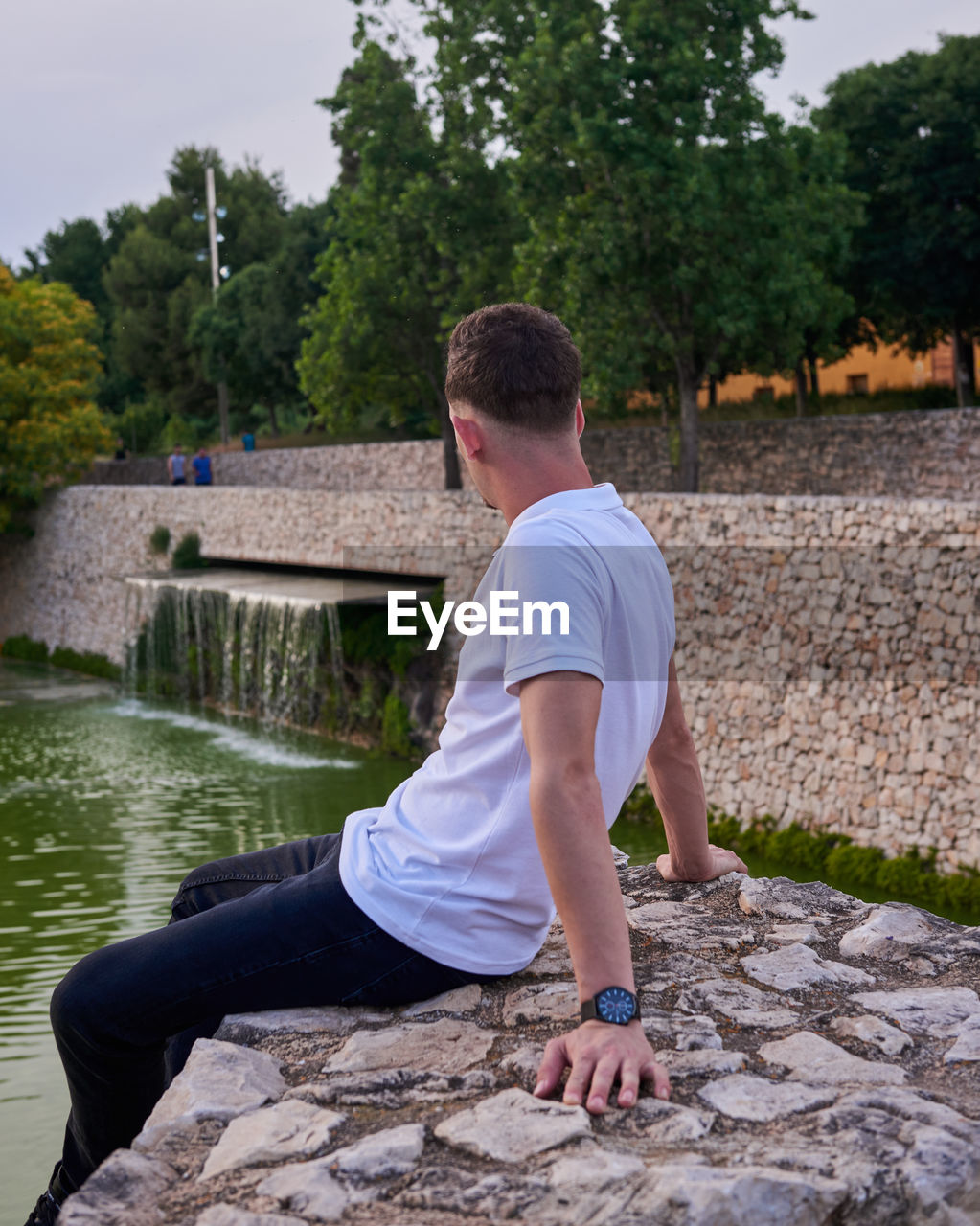 Side view of man sitting on retaining wall