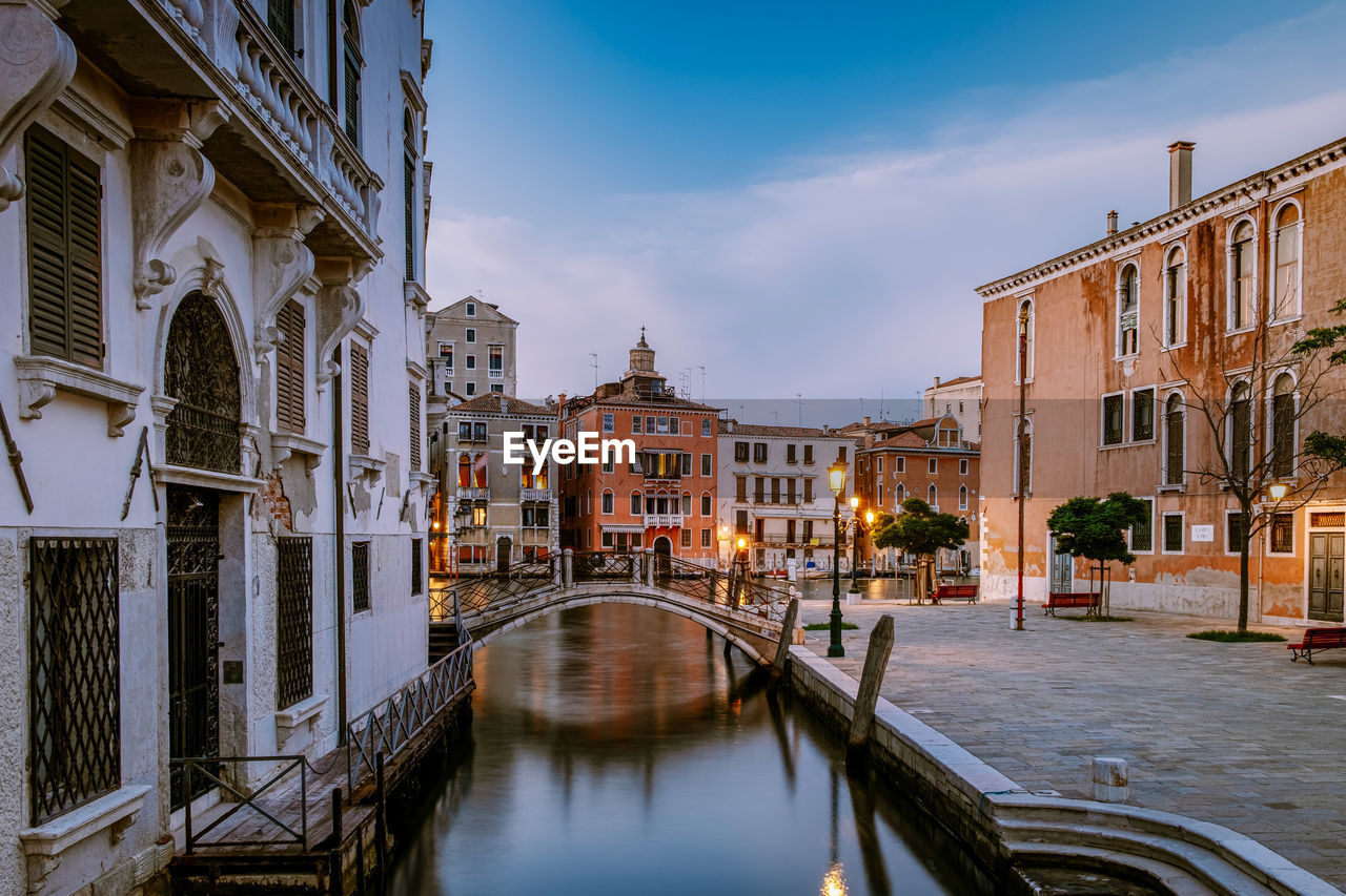 BRIDGE OVER CANAL BY BUILDINGS AGAINST SKY IN CITY