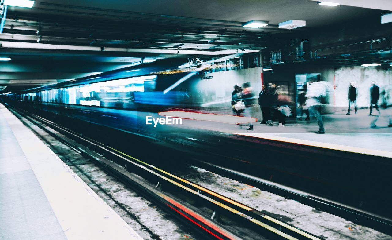 People by blurred motion of train at illuminated railroad station