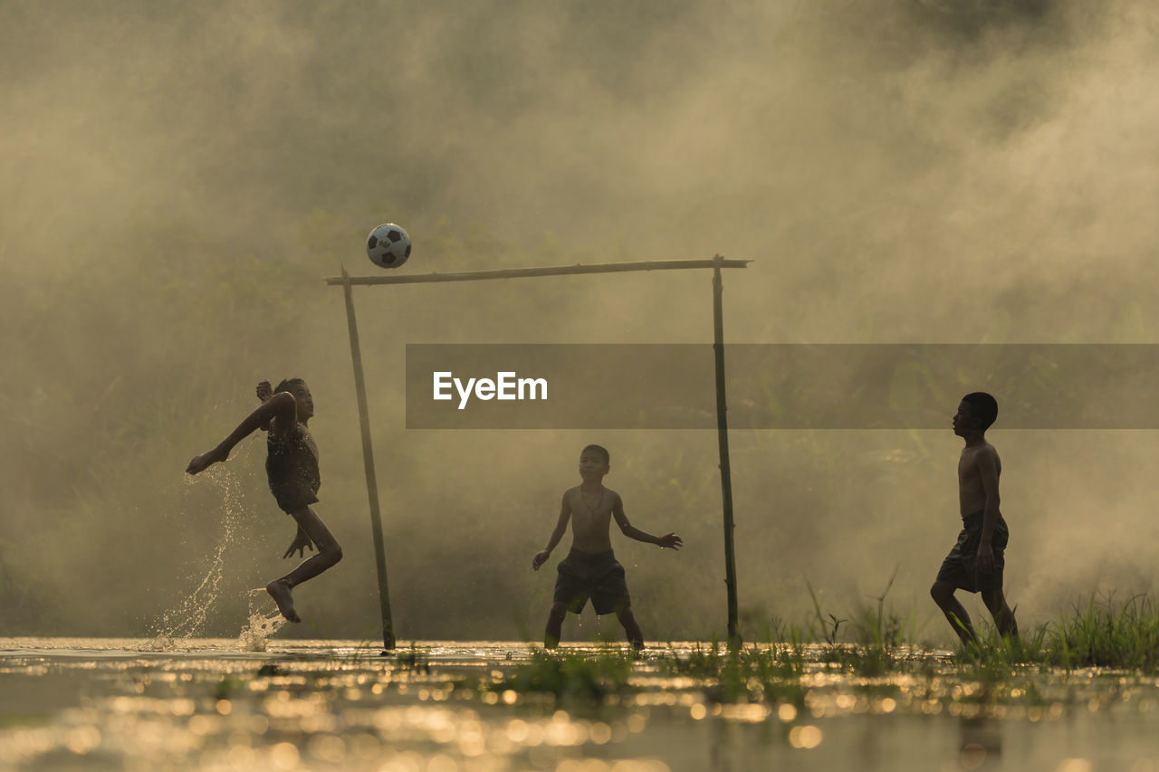 Shirtless boys playing soccer on wet field during monsoon