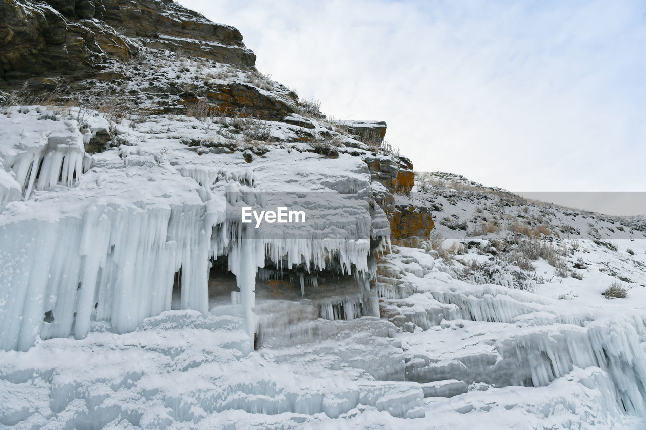 Icicles on snow covered land against sky