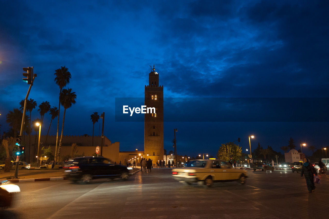 Cars on road by illuminated buildings against sky at night