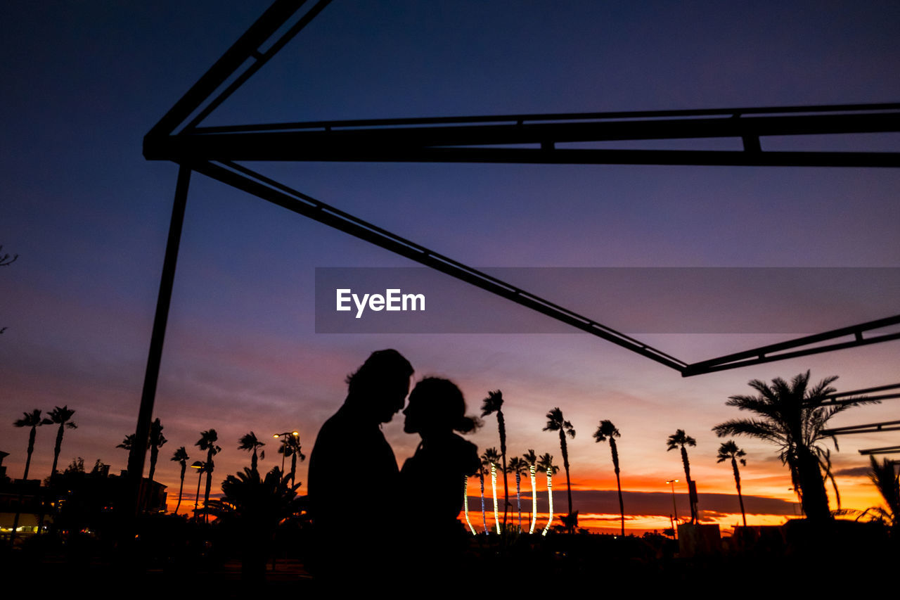 Silhouette couple romancing in park at sunset