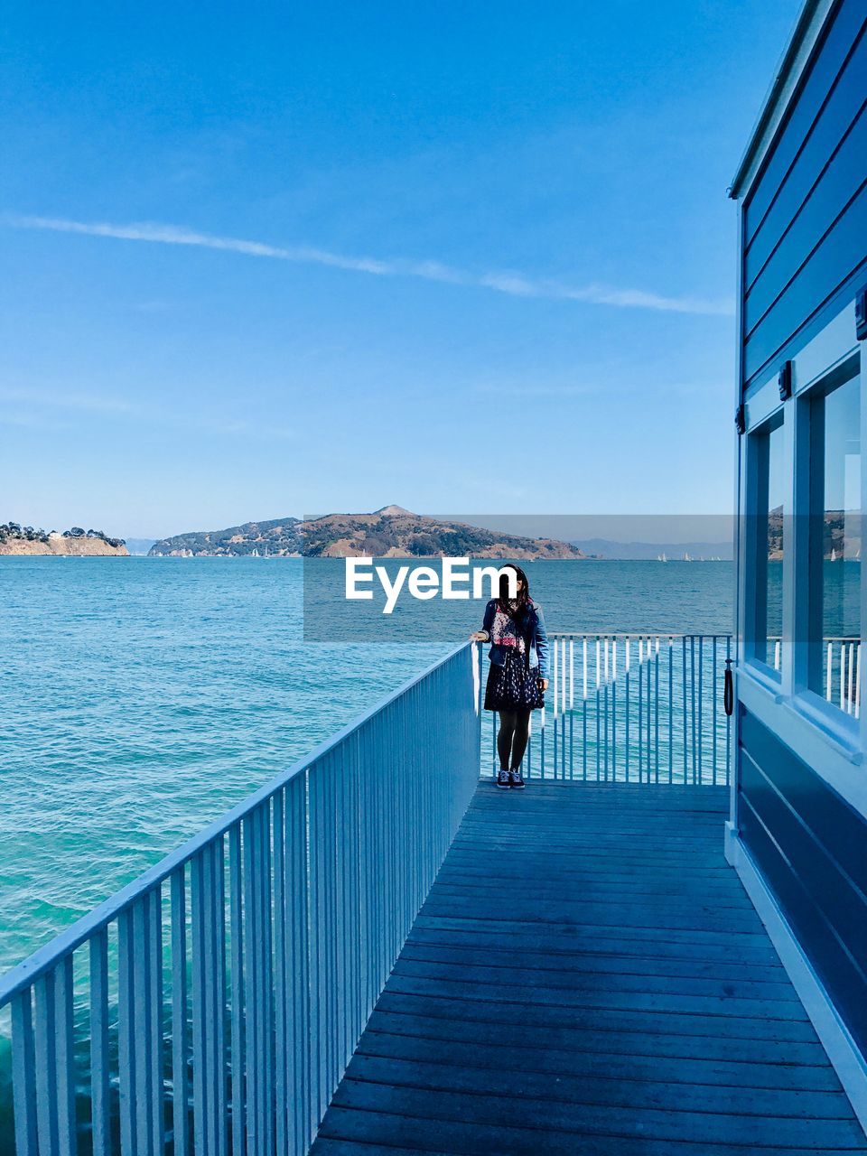 Portrait of young woman standing by railing against sea