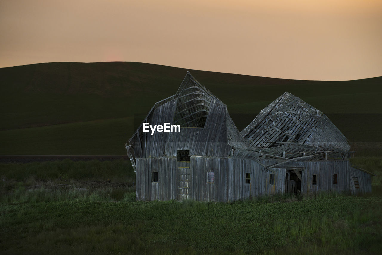 Abandoned barn on grassy field against clear sky during sunset