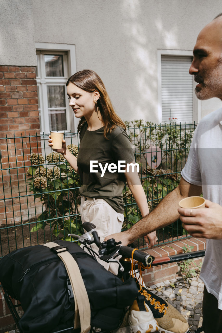 Young woman with male friend wheeling with bicycle while having coffee