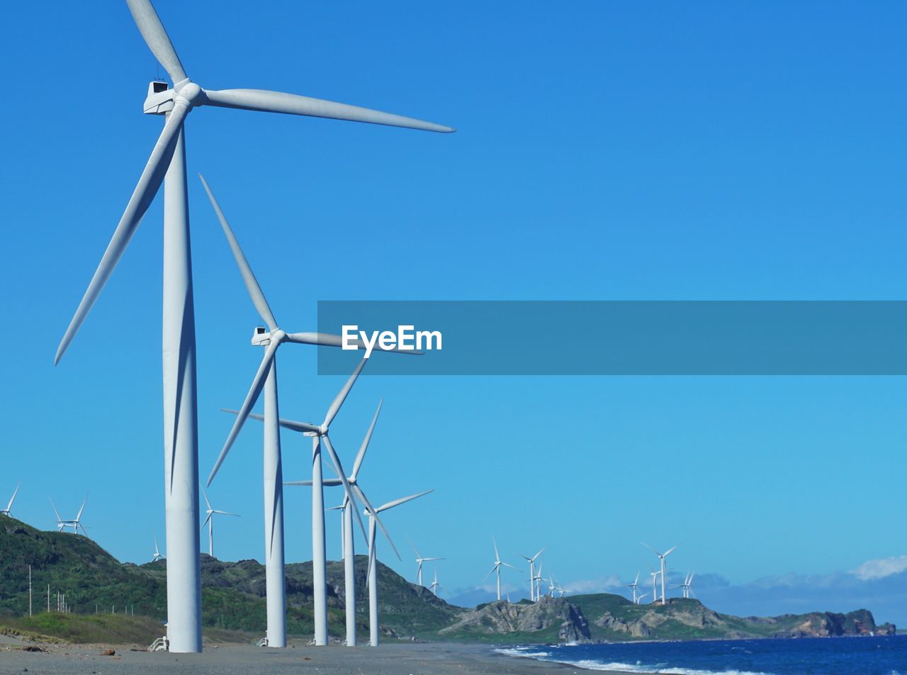 Wind turbines on landscape against clear blue sky