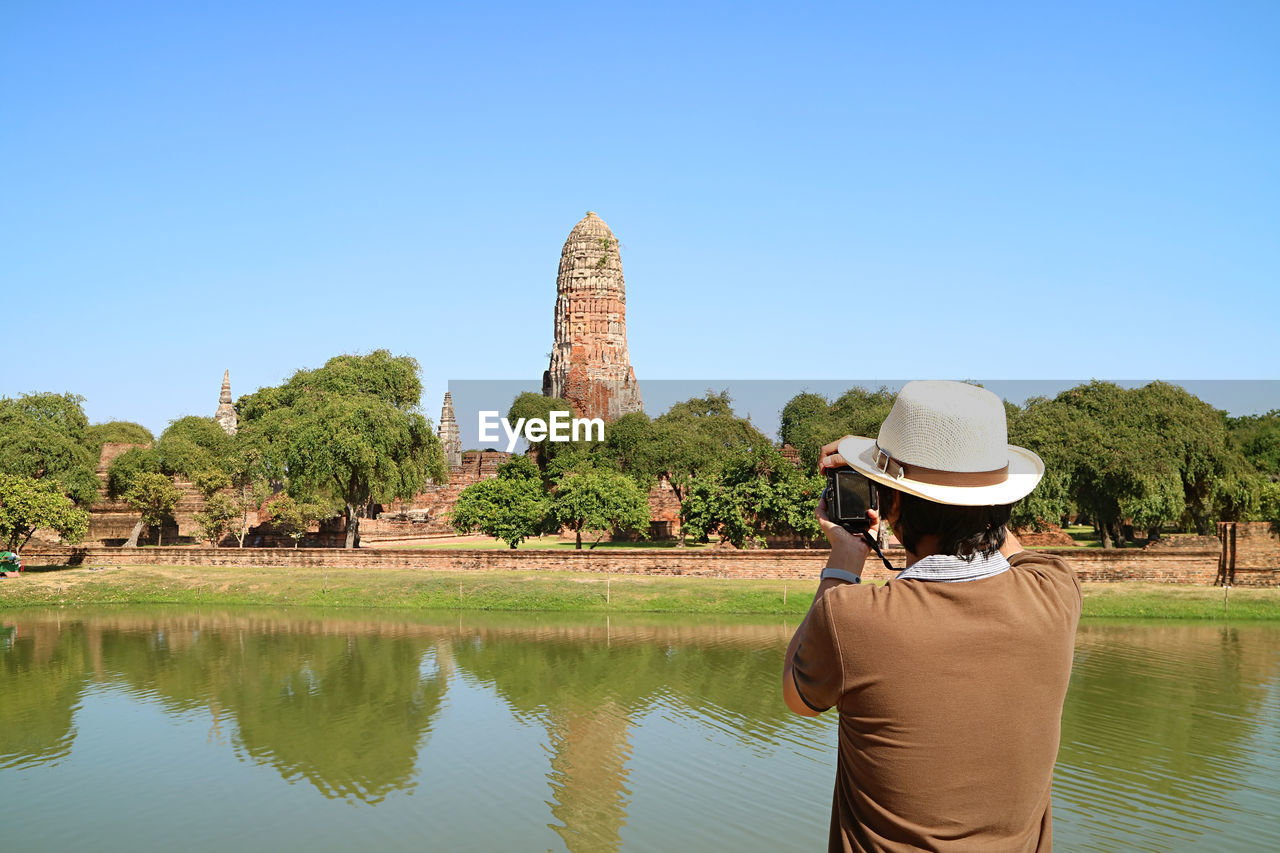 Man taking photos of the medieval prang of wat phra ram temple ruins in ayutthaya, thailand