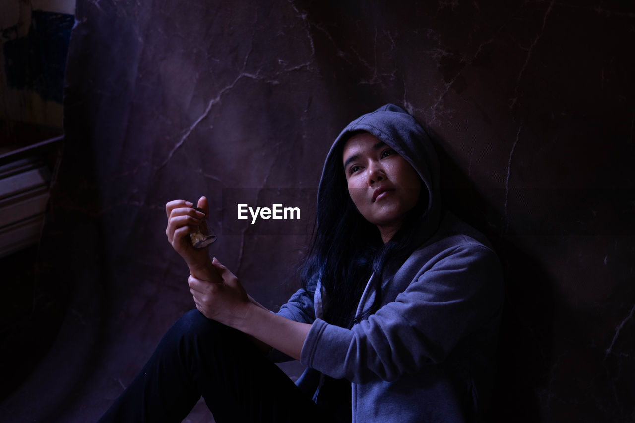 Woman wearing hooded shirt sitting against wall