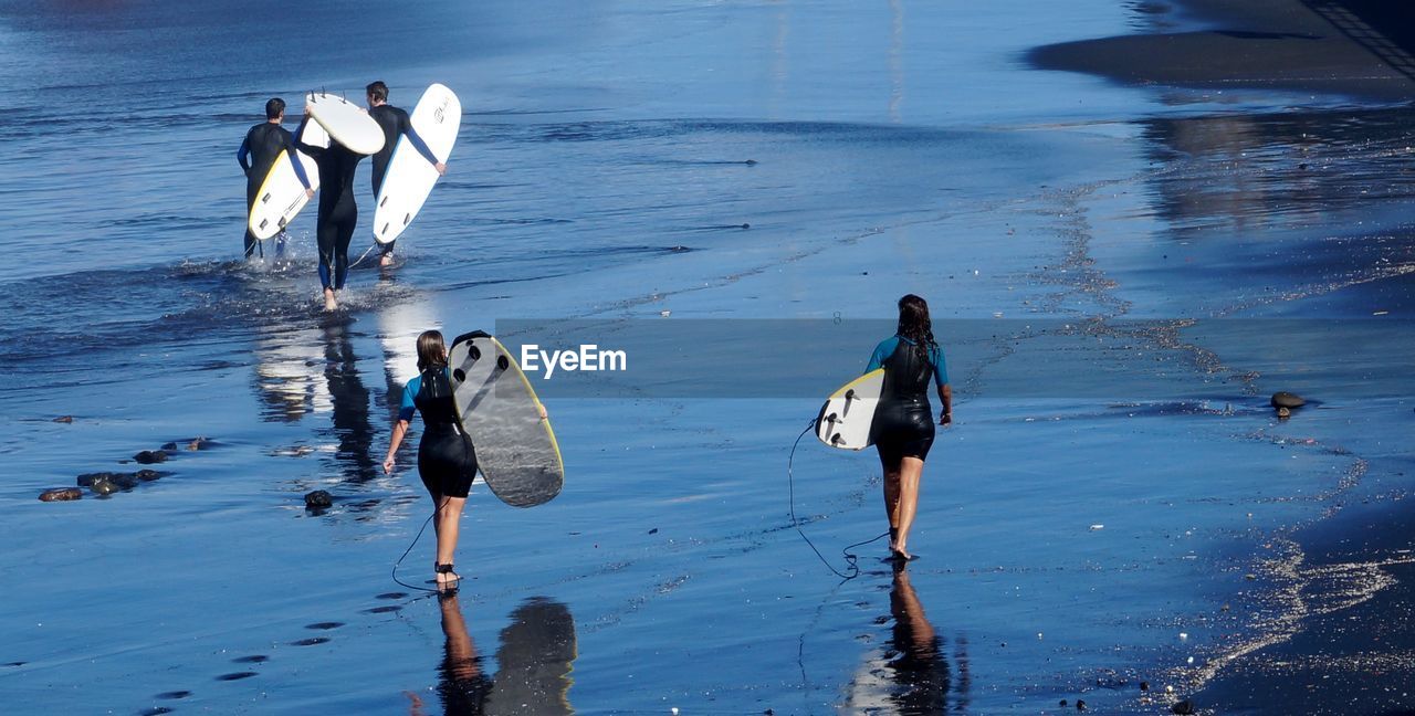 Rear view of surfers carrying surfboard on shore