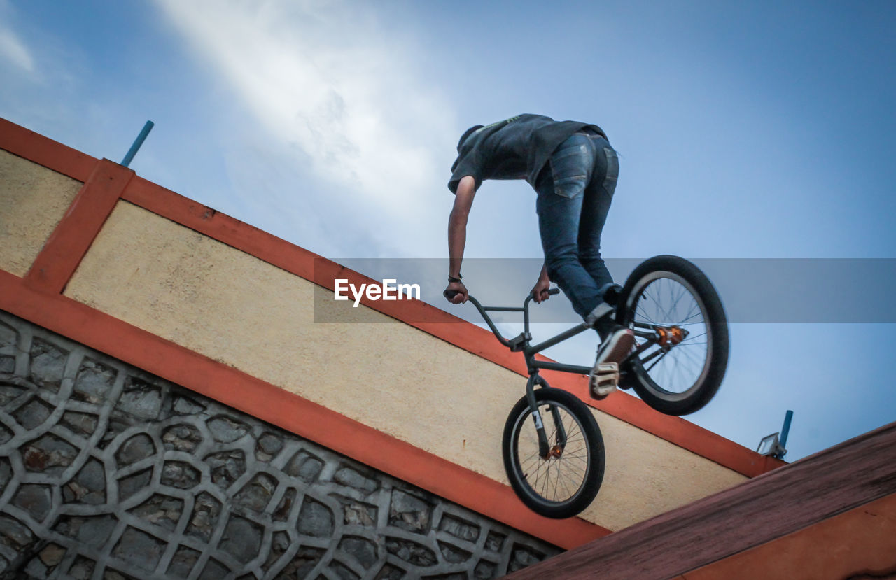 Low section of man performing stunt on bicycle against blue sky