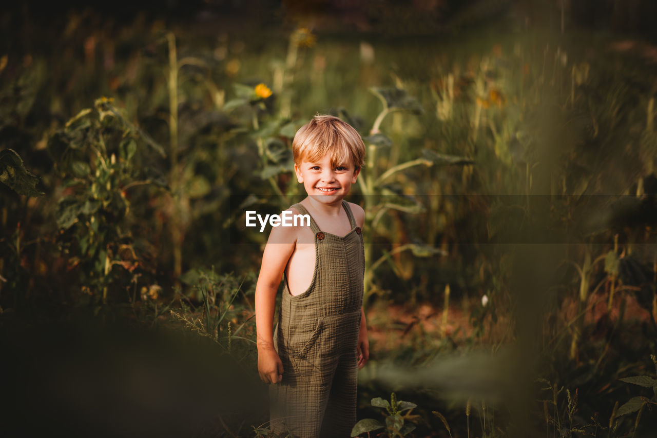 Cute young boy in dungarees in a field smiling at the camera