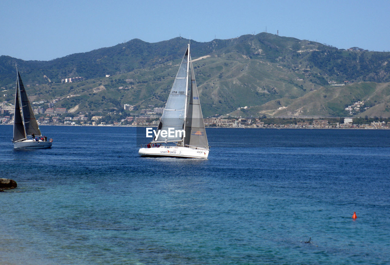 SAILBOAT SAILING ON SEA AGAINST MOUNTAIN