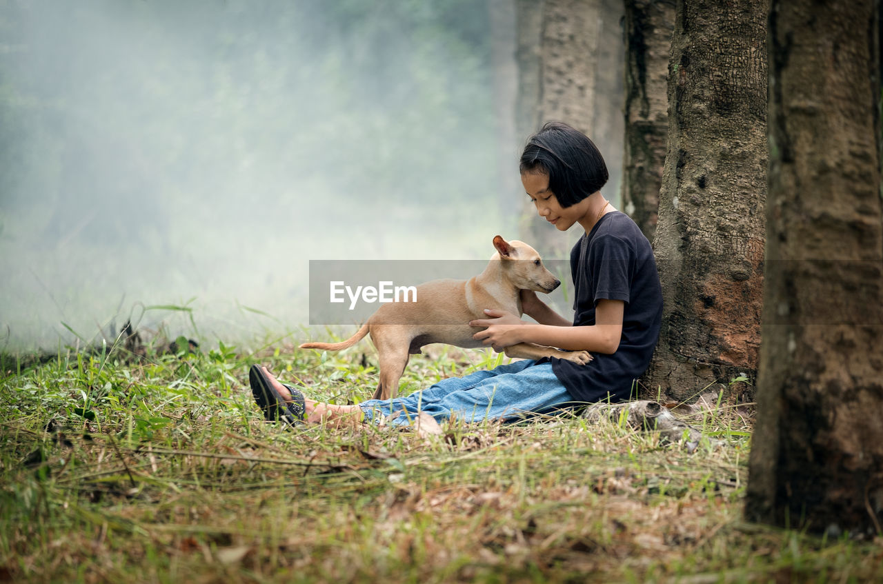 Side view of girl sitting with dog at forest