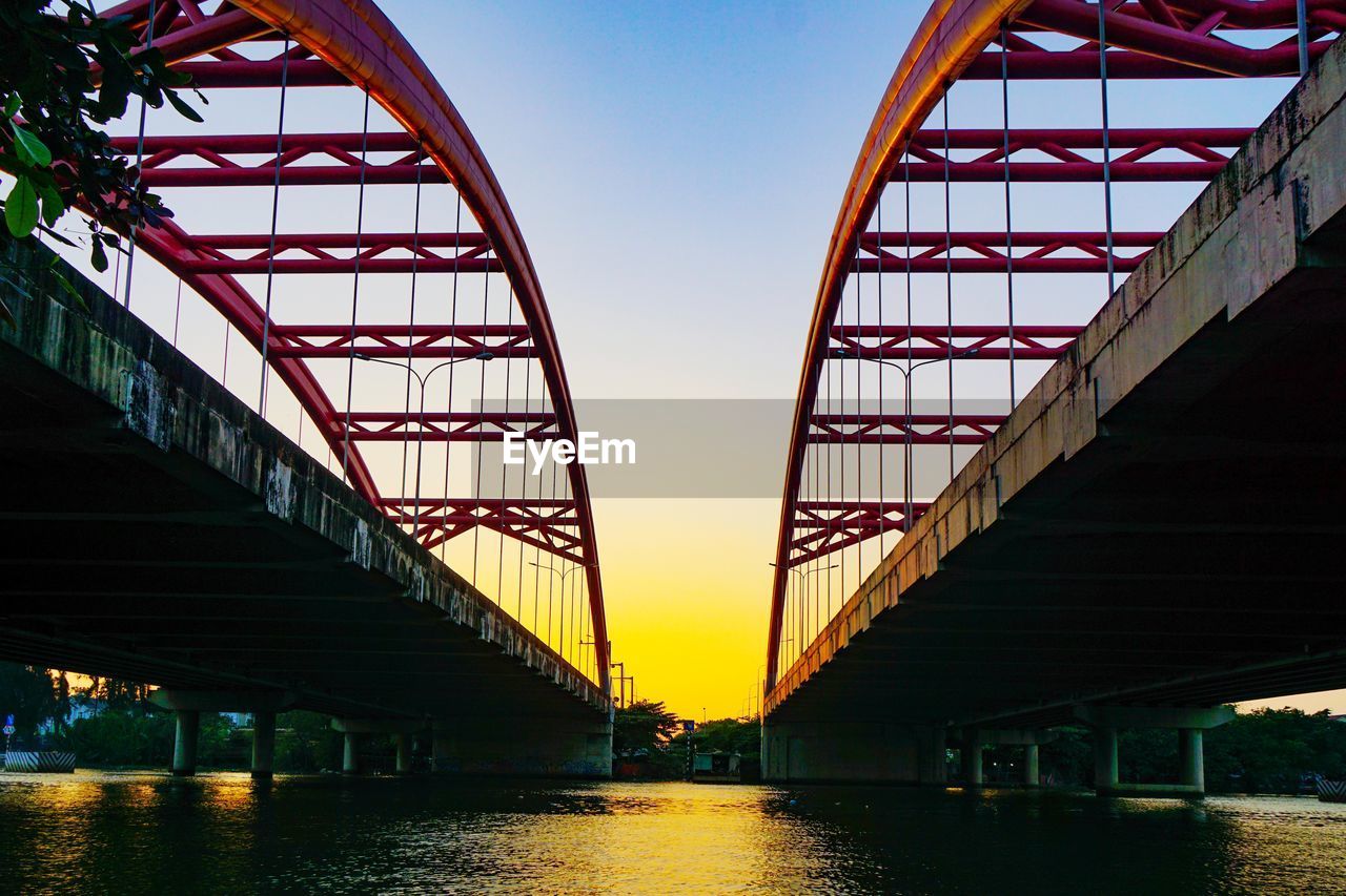 LOW ANGLE VIEW OF BRIDGE OVER RIVER DURING SUNSET