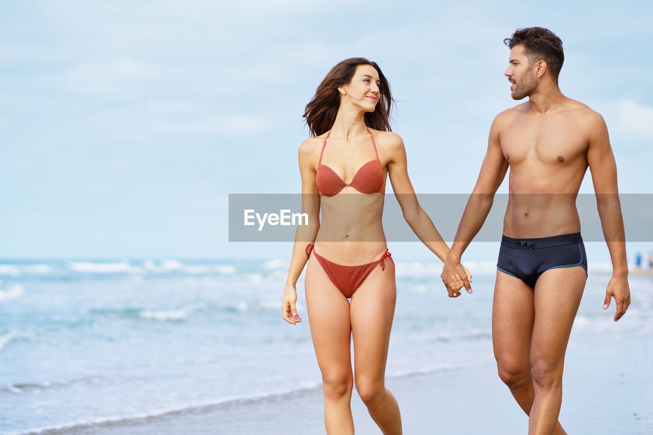 Young couple standing at beach against sky