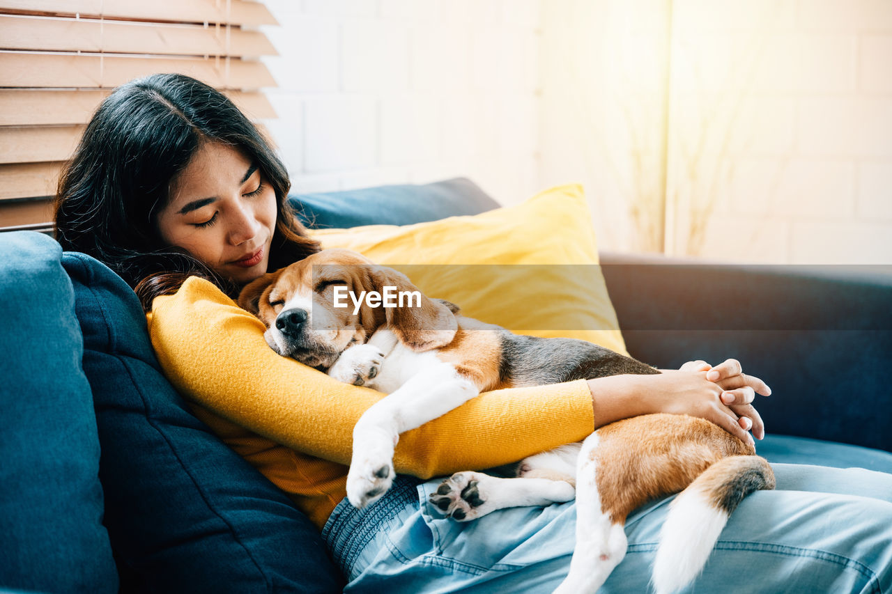 portrait of young woman with dog relaxing on sofa at home