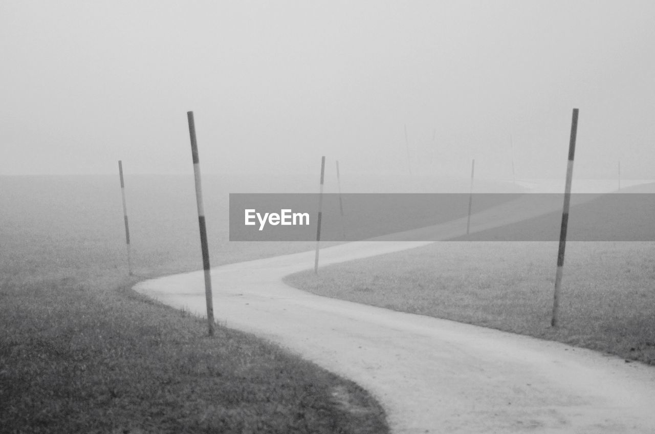 Street amidst grassy field in foggy weather