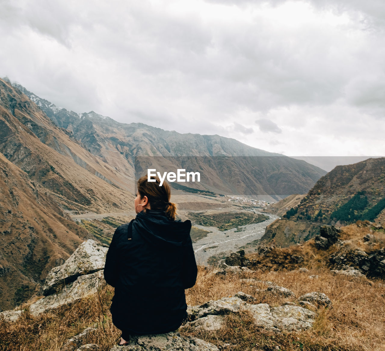 Rear view of woman sitting on mountain against sky