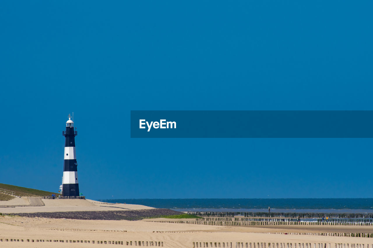 Lighthouse by sea against clear sky