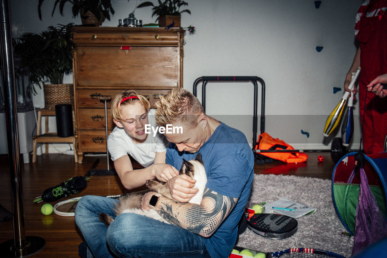 Father and son stroking cat in living room