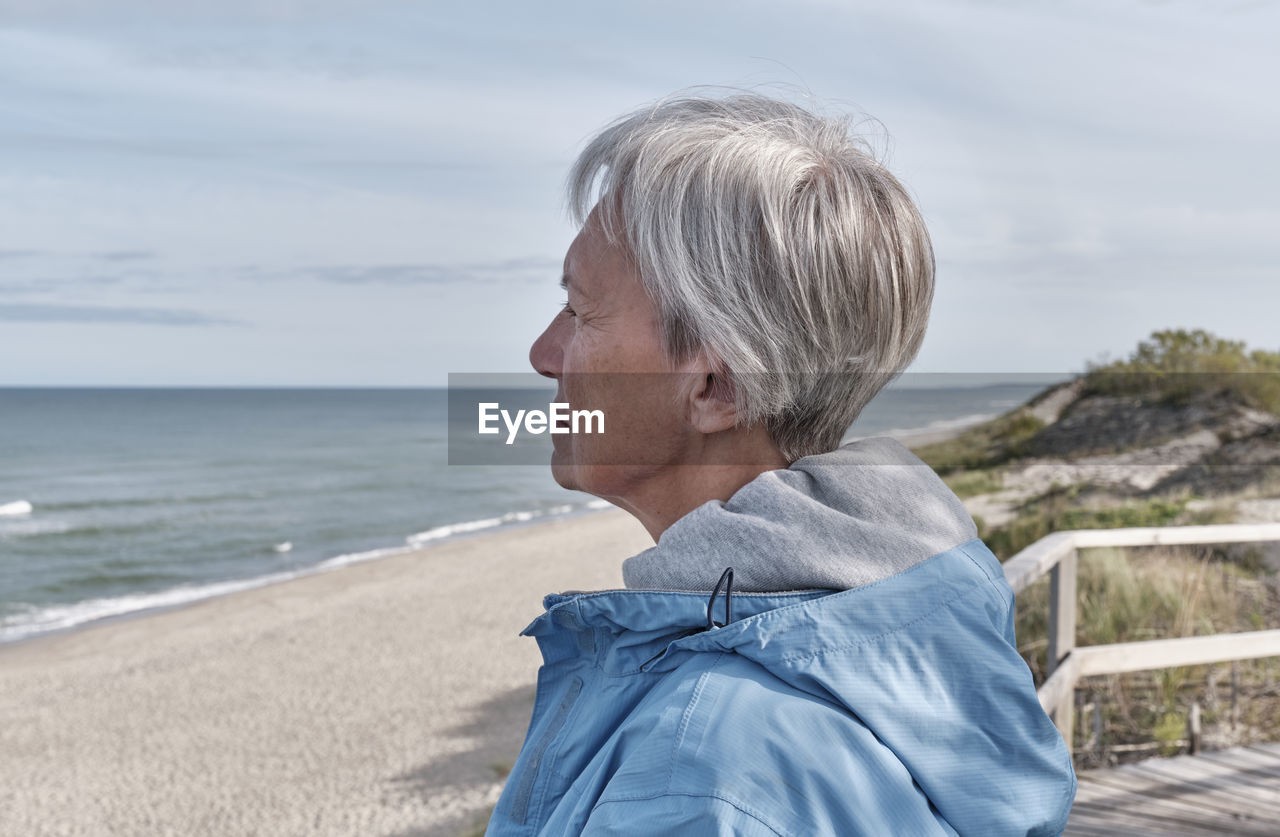 Serious senior woman with short gray hair standing on by sea and looking into distance. close-up