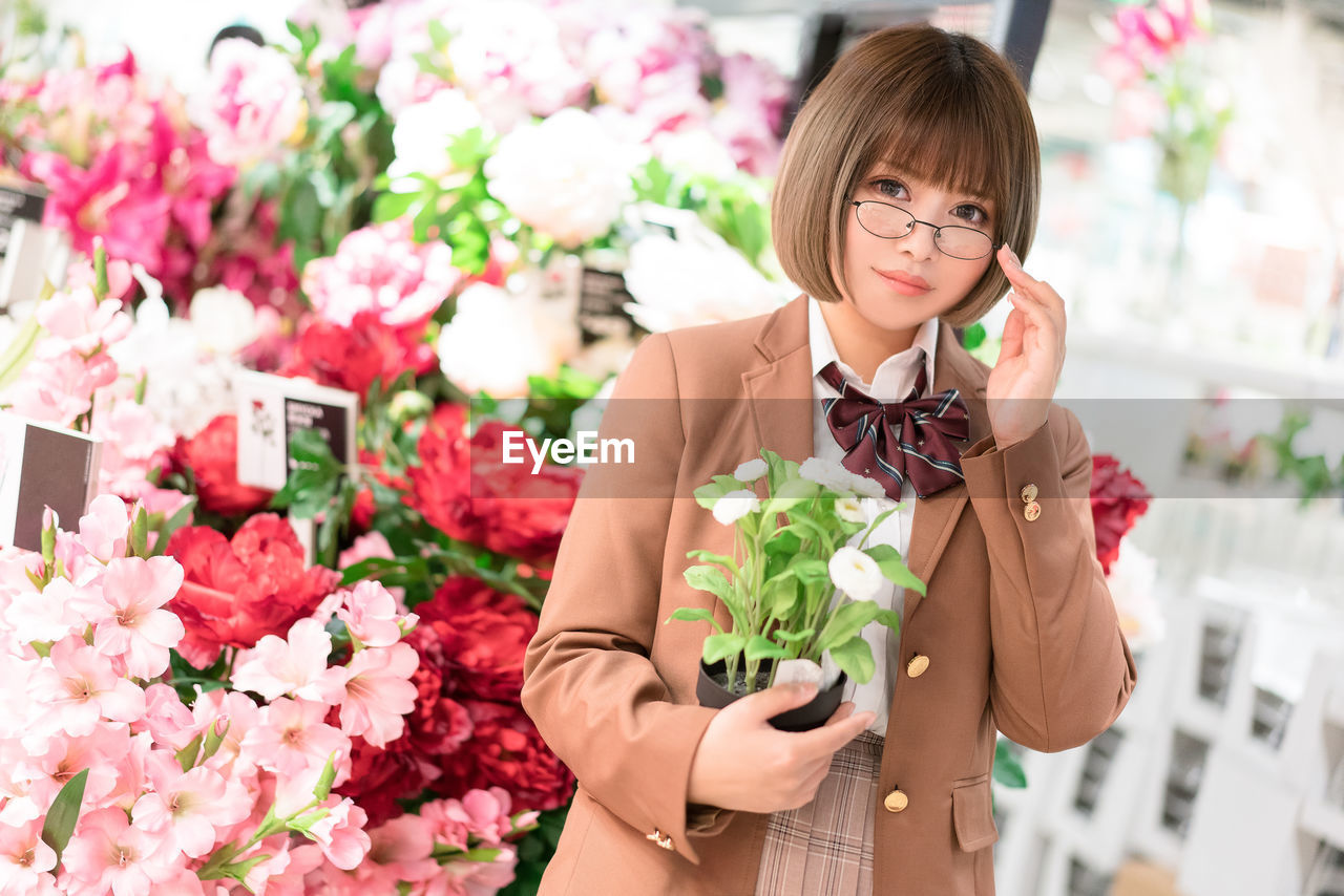 Portrait of woman holding plant standing at flower shop