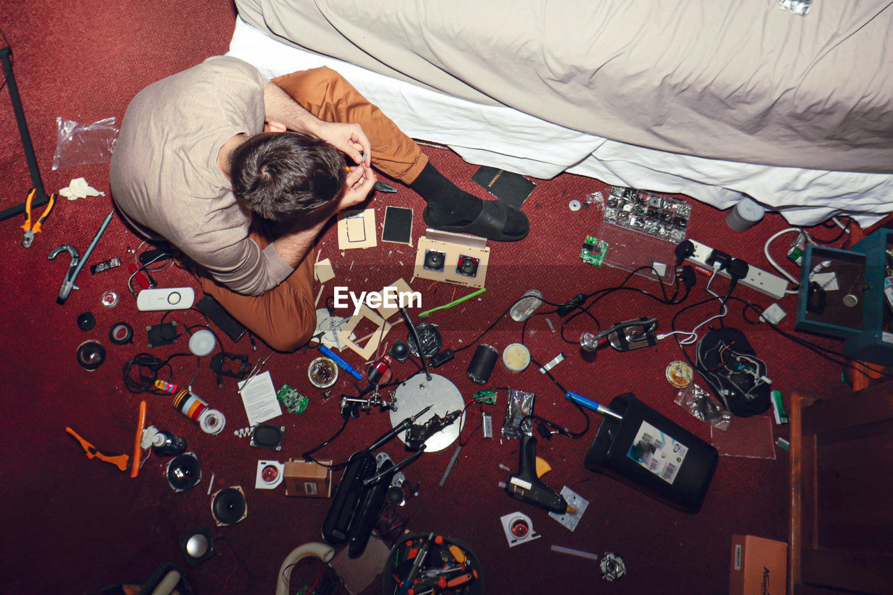 High angle view of young man sitting on the floor surrounded by gadgets 