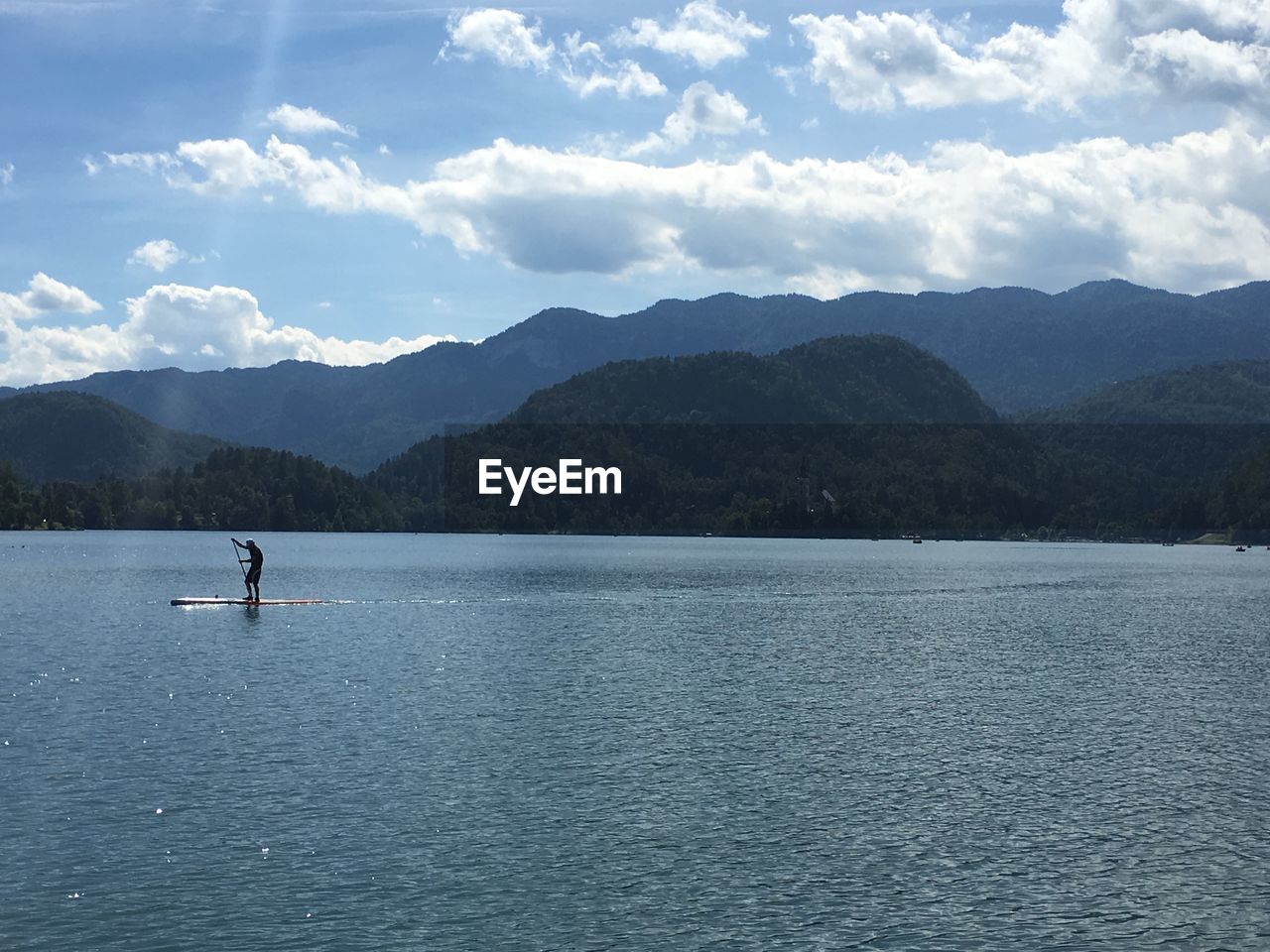 Scenic view of person paddle boarding on lake and mountains against sky