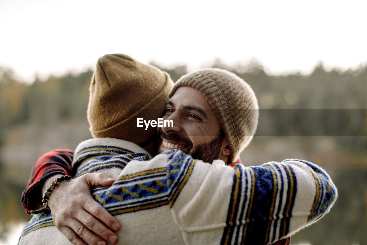 Happy male friends embracing each other wearing knit hats