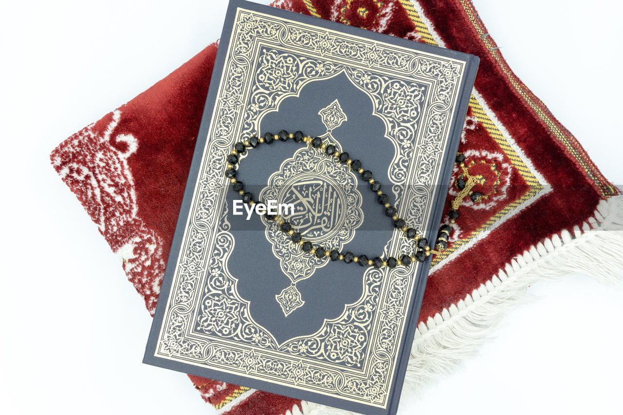 Quran, rosary and prayer mat over white background