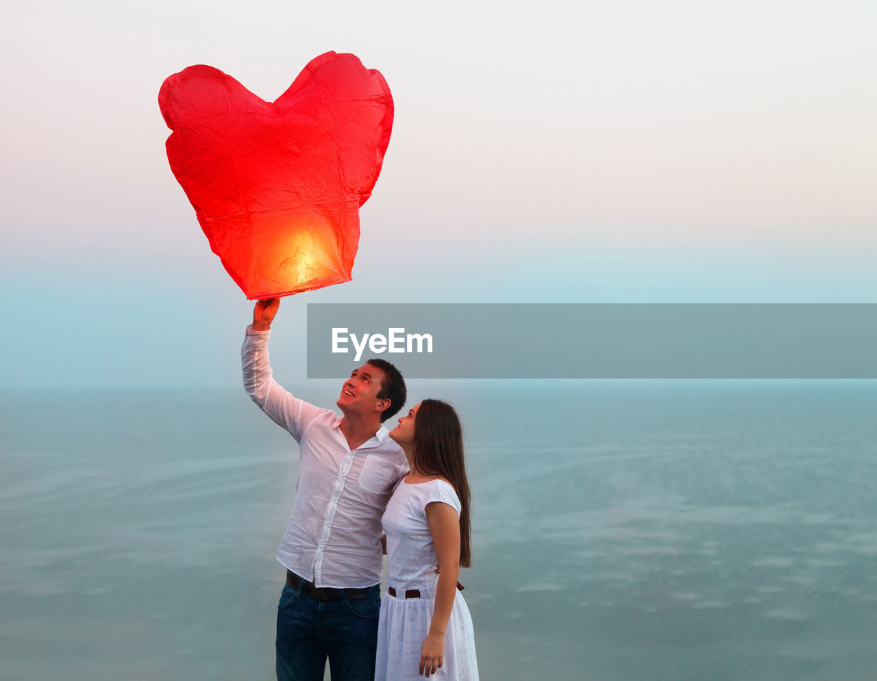 WOMAN WITH HEART SHAPE STANDING AGAINST SEA