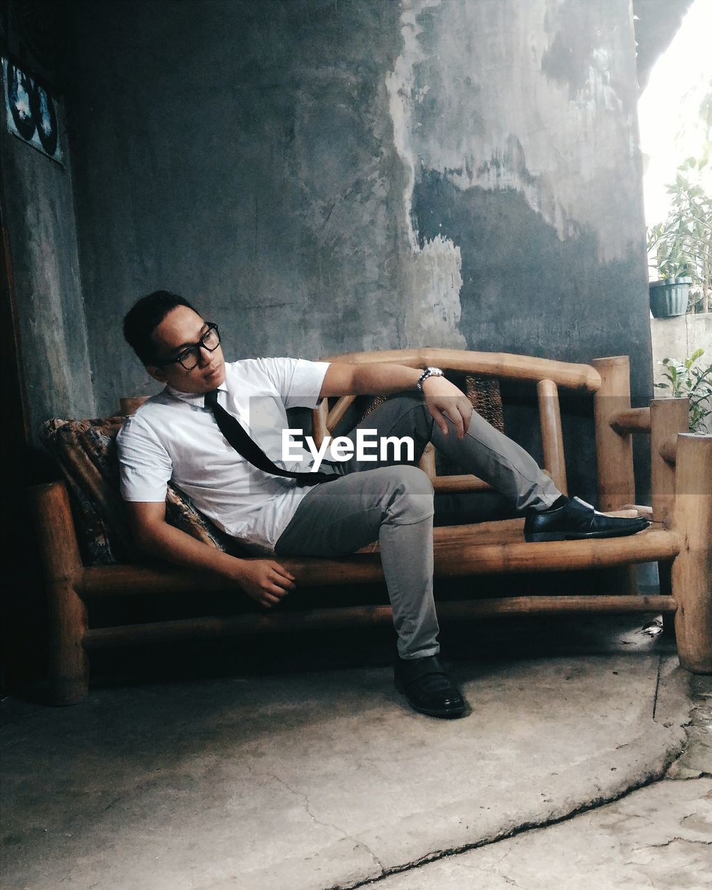 Man looking away while sitting on bench against wall