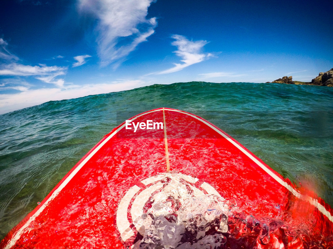 Red surfboard in sea against sky on sunny day