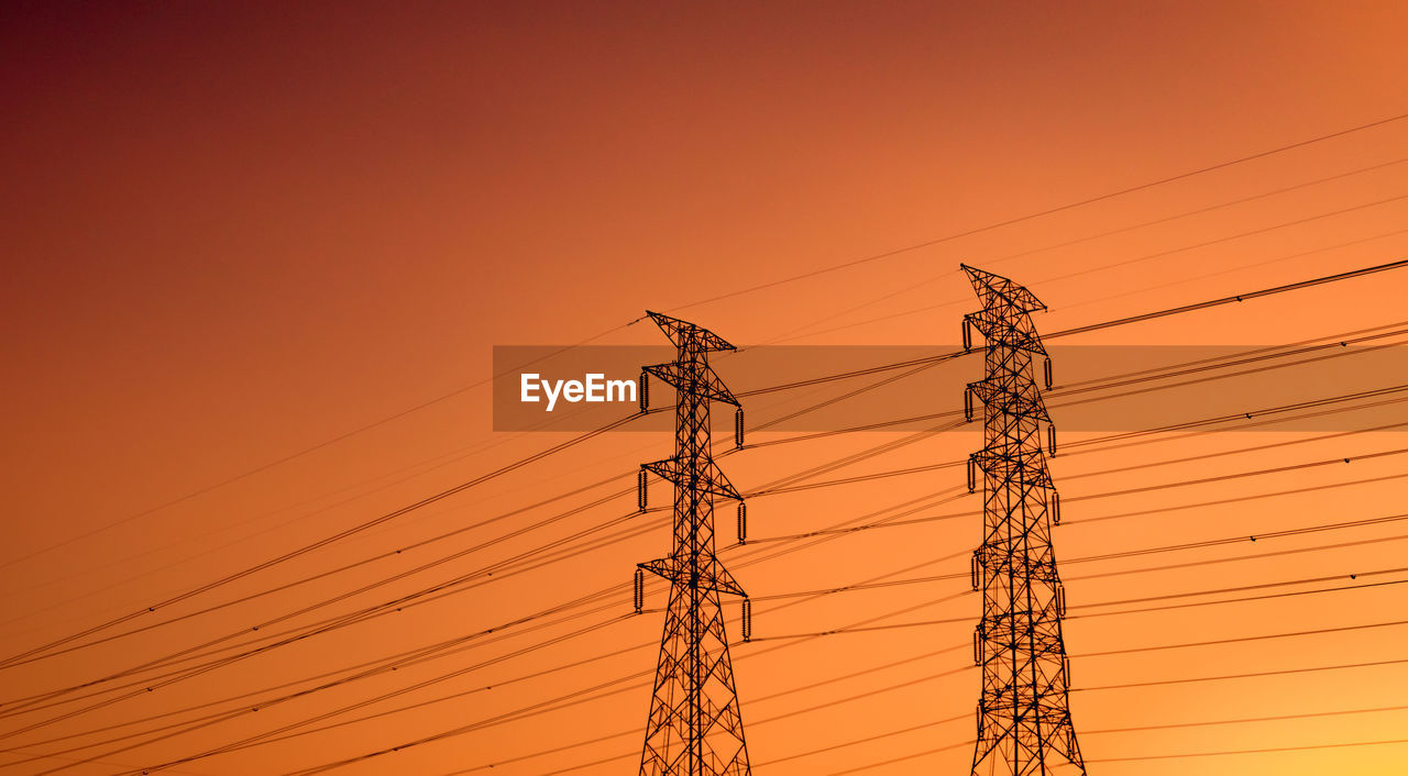 Low angle view of electricity pylon against orange sky. high voltage electric pole.