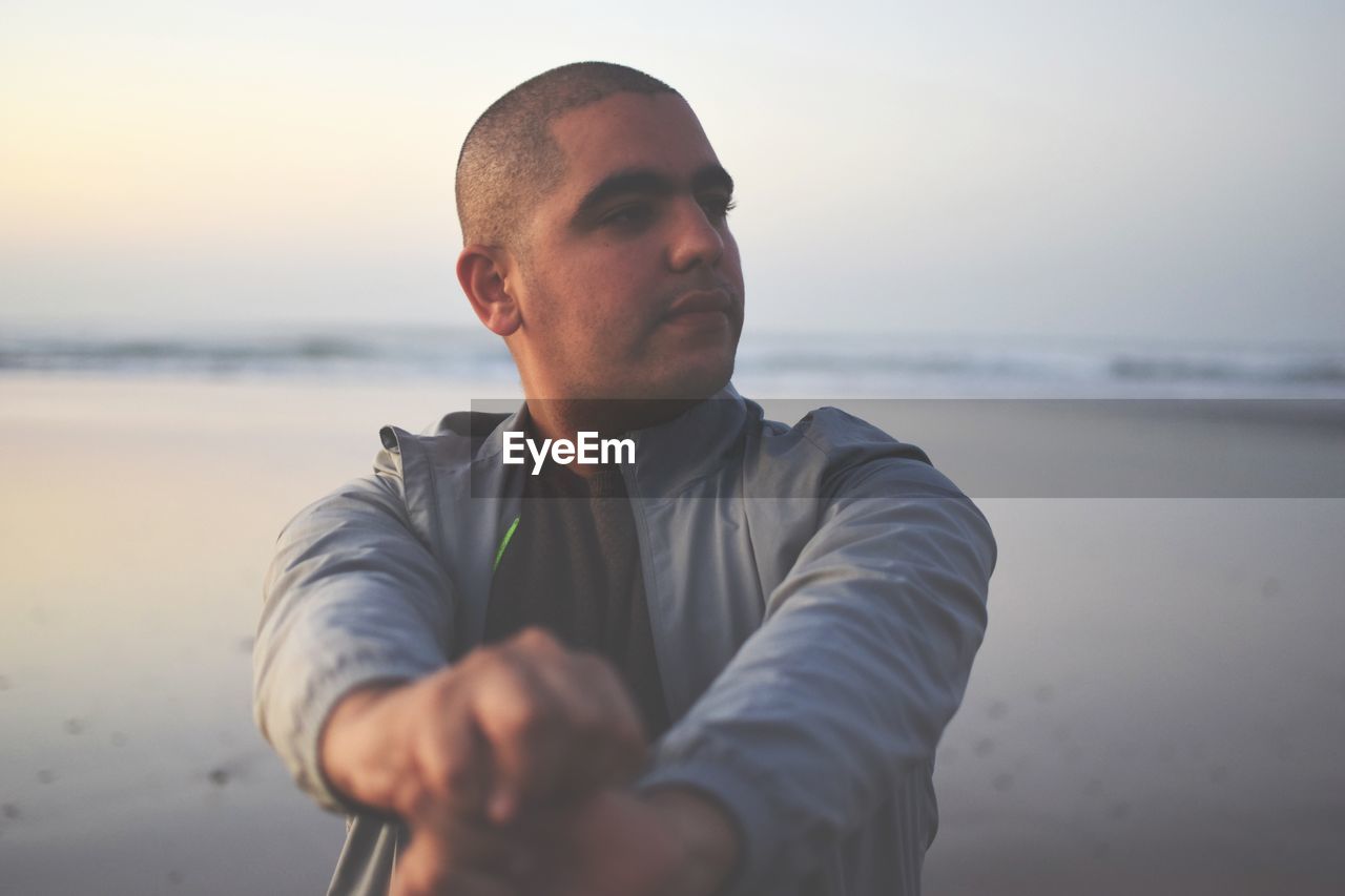 Thoughtful man standing at beach during sunset