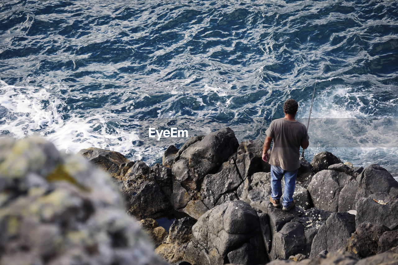 Rear view of man standing on rock at sea