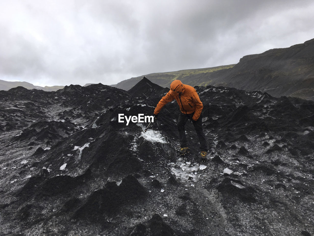 Man breaking ice on mountain against cloudy sky