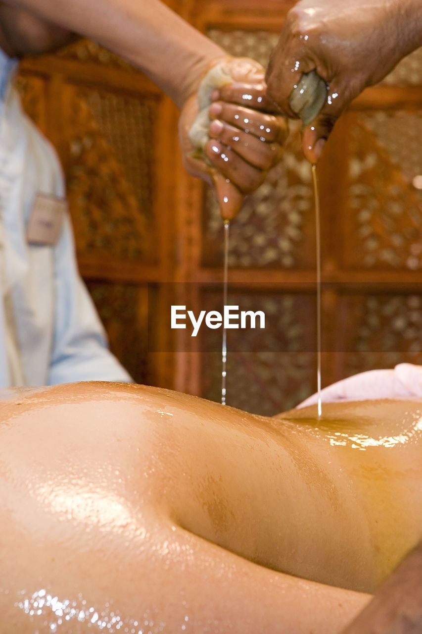 Cropped hands pouring oil on woman back in beauty spa