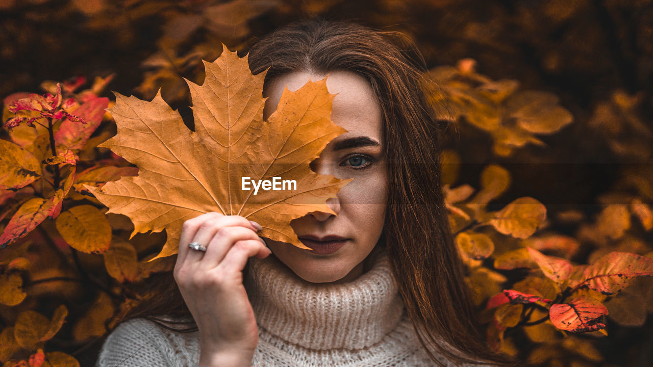 Close-up of beautiful woman holding maple leaf against face during autumn