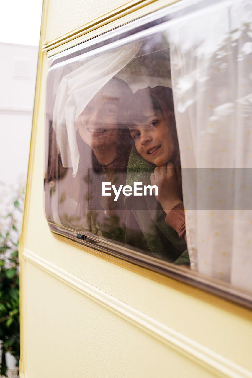 Children smiling while looking outside from the cabin of a motorhome