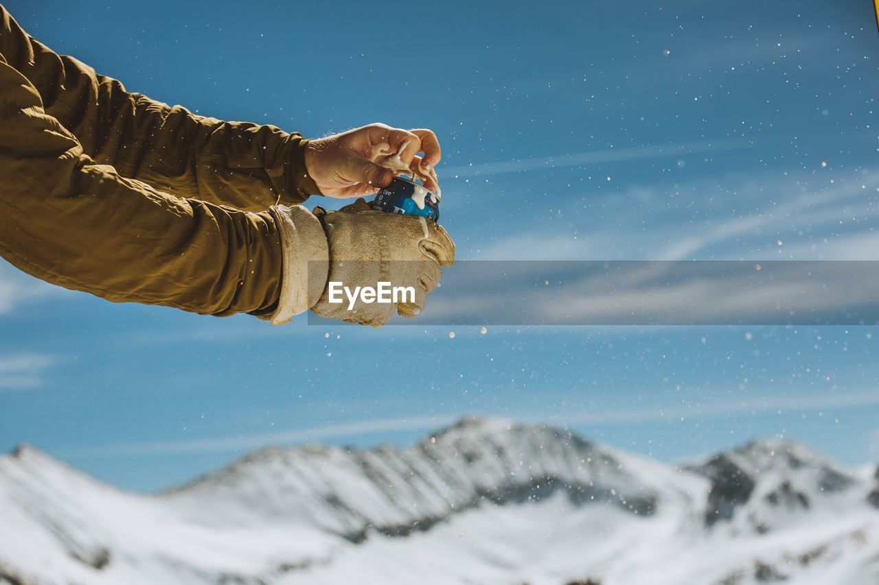 LOW SECTION OF PERSON ON SNOWCAPPED MOUNTAINS AGAINST SKY