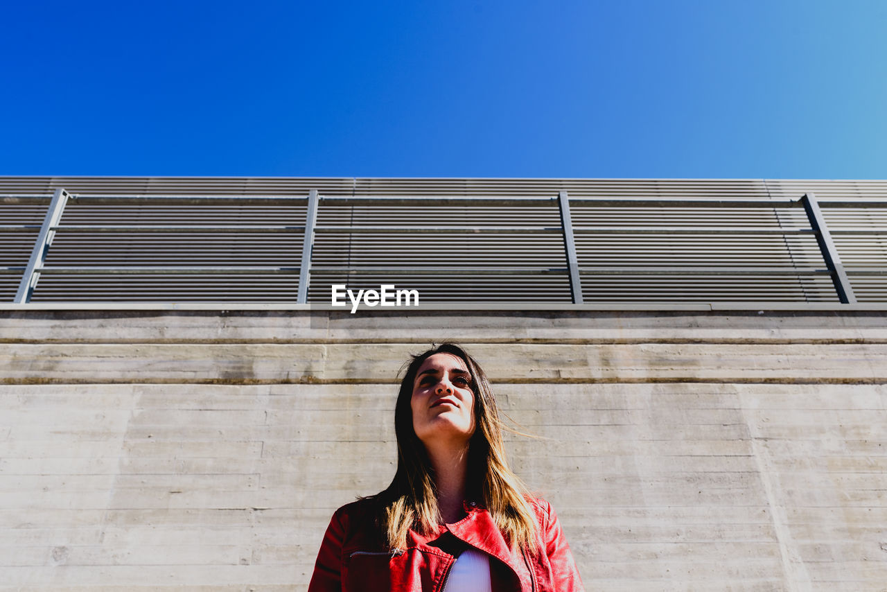 Low angle view of young woman standing against wall