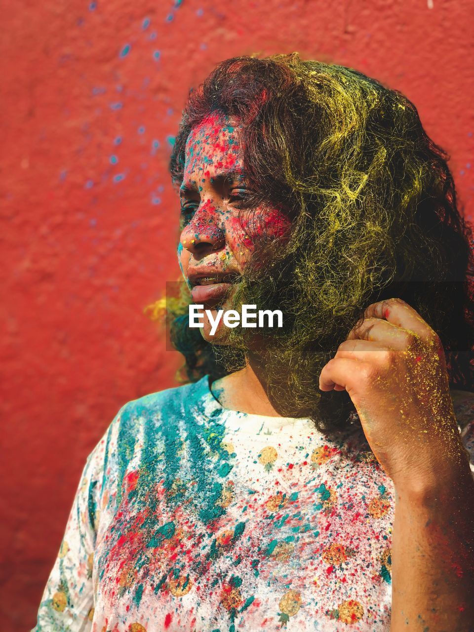 Woman with multi colored powder paint on face against wall during festival