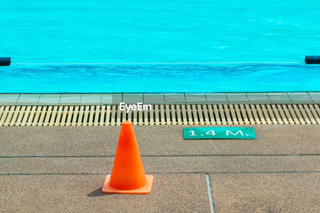 Orange cone and depth mark sign at a poolside of a local swimming pool